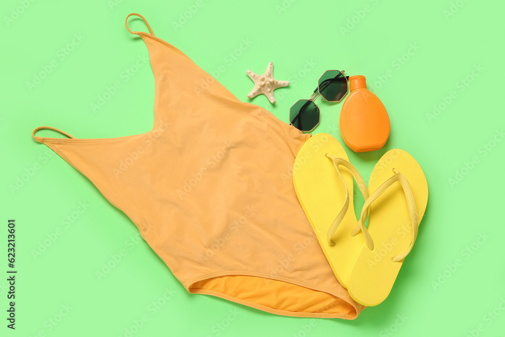 Bright swimsuit, flip-flops, sunglasses, bottle of sunscreen cream and starfish on color background