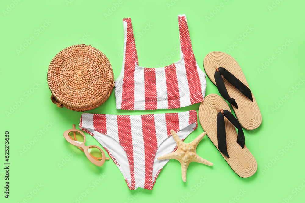 Stylish swimsuit, flip-flops, sunglasses, bag and starfish on green background