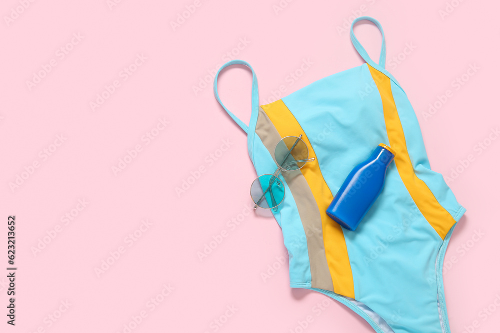 Stylish swimsuit, sunglasses and bottle of sunscreen cream on pink background