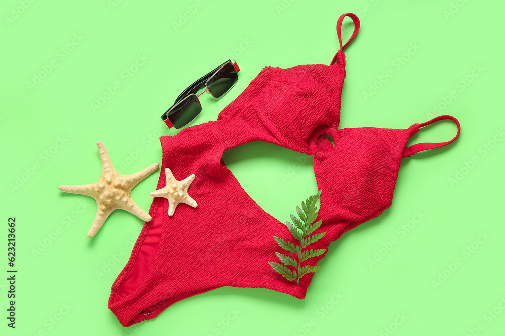 Stylish swimsuit, sunglasses, fern leaf and starfishes on green background