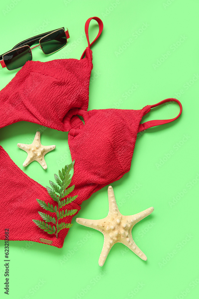 Stylish swimsuit, sunglasses, fern leaf and starfishes on green background