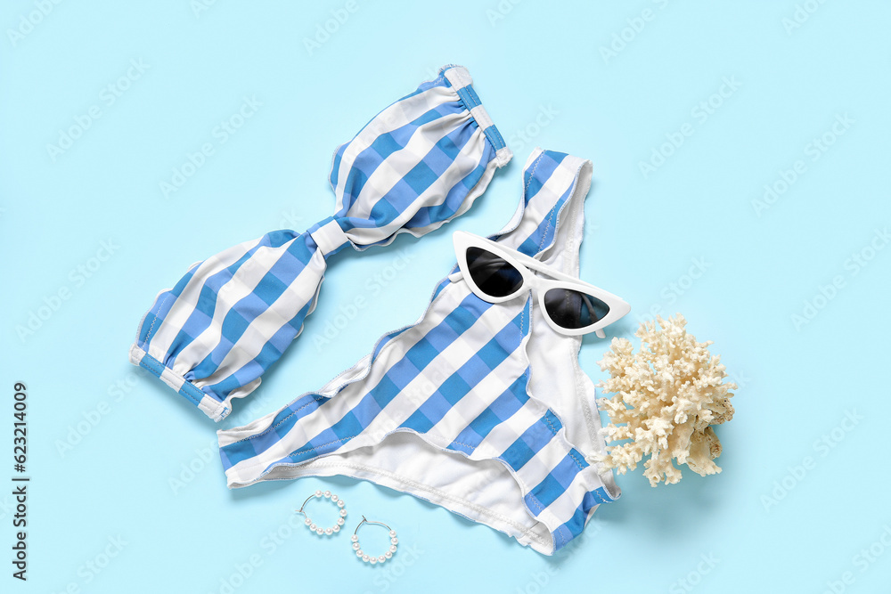 Stylish swimsuit, sunglasses, earrings and coral on color background