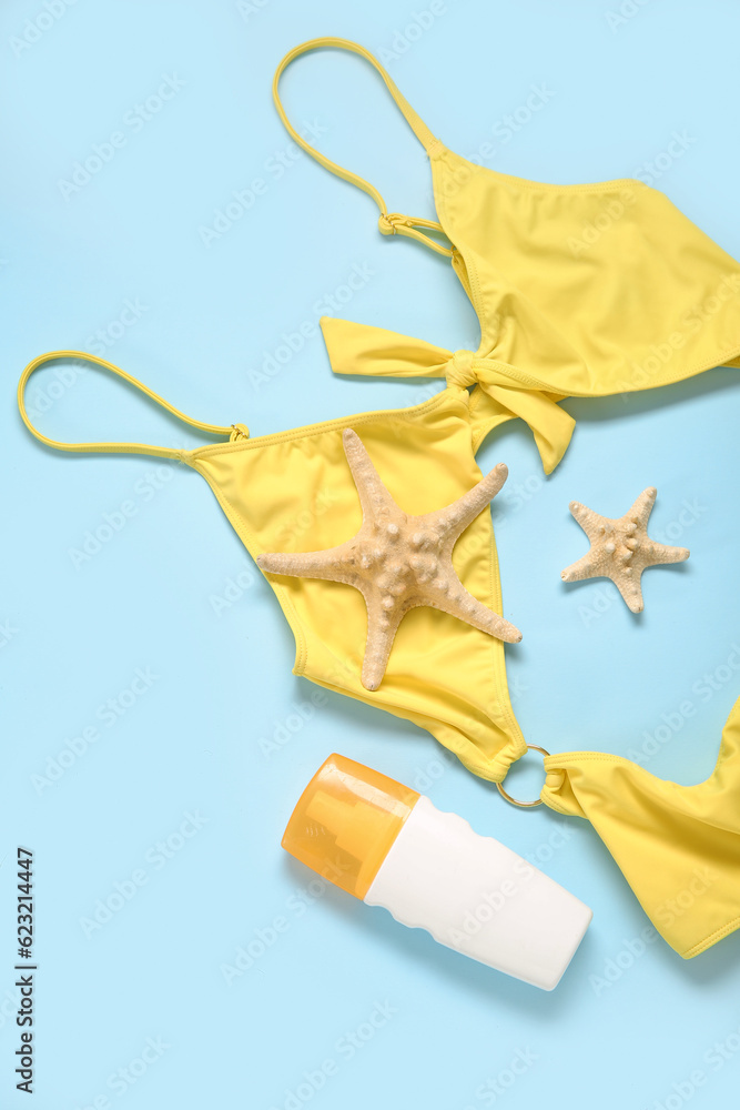 Stylish swimsuit, bottle of sunscreen cream and starfishes on color background