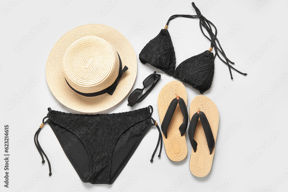 Stylish swimsuit, hat, sunglasses and flip-flops on light background