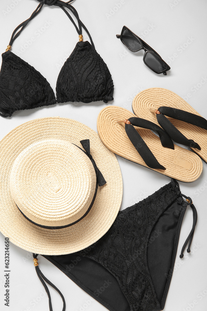 Stylish swimsuit, hat, sunglasses and flip-flops on light background, closeup