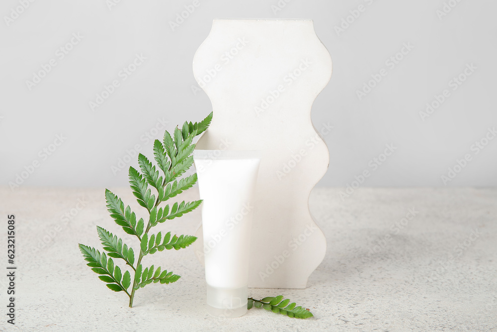 Composition with tube of cosmetic product, plaster podium and fern leaf on light background