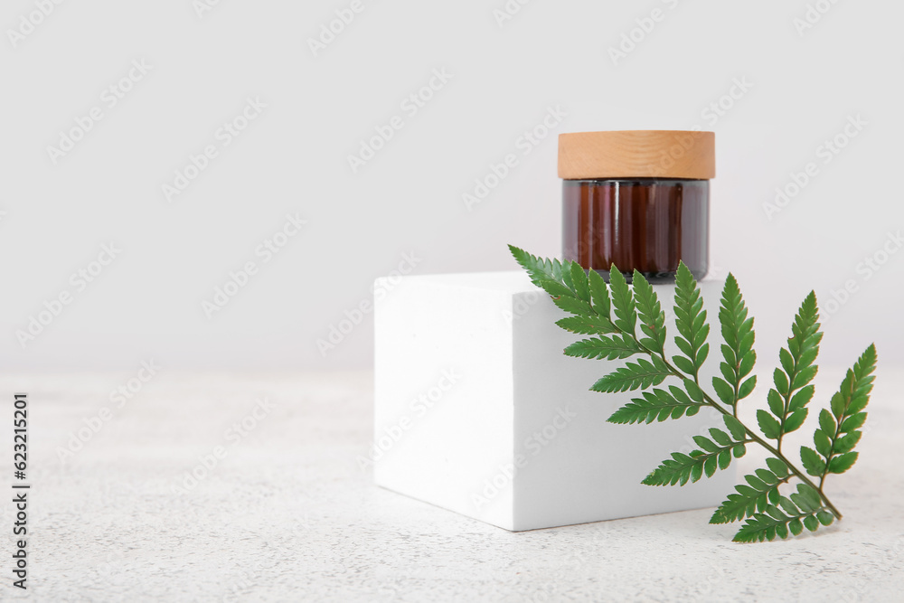 Jar of cosmetic product, plaster podium and fern leaf on light background