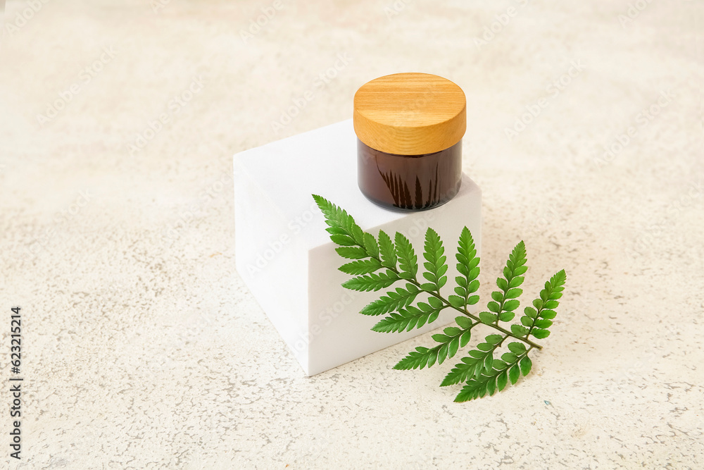 Jar of cosmetic product, plaster podium and fern leaf on light background