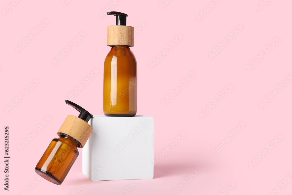 Bottles of cosmetic products and plaster podium on pink background