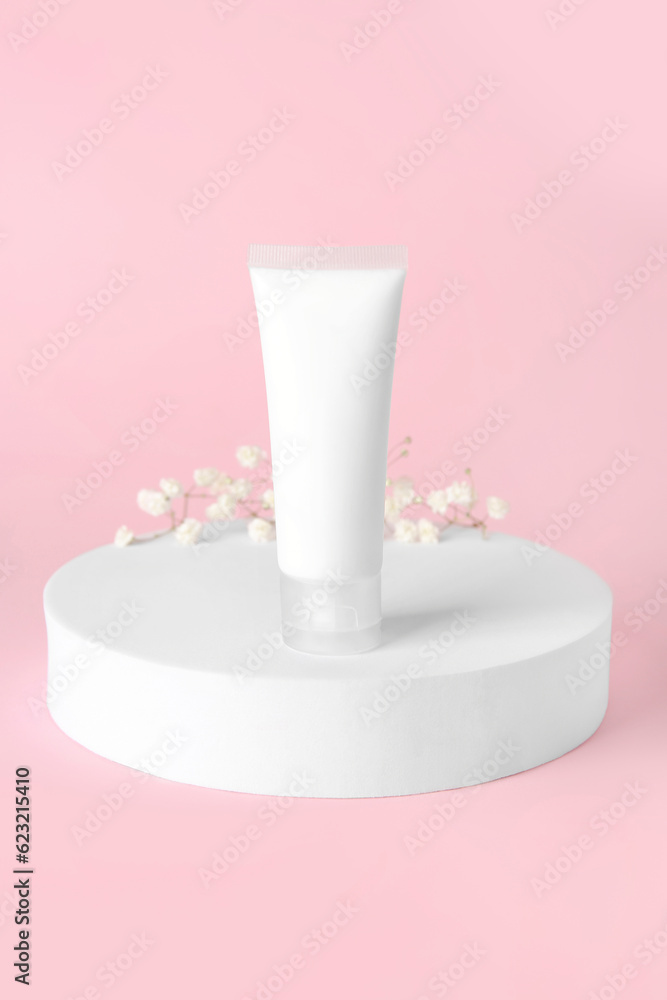 Plaster podium with tube of cosmetic product and gypsophila flowers on pink background