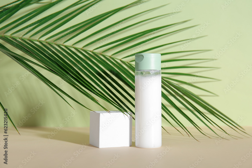 Bottle of cosmetic product, plaster podium and palm leaf on green background