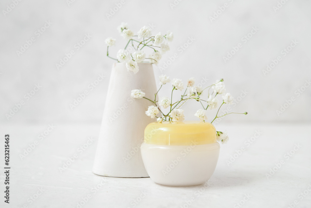 Composition with jar of cosmetic product, plaster podium and gypsophila flowers on light background