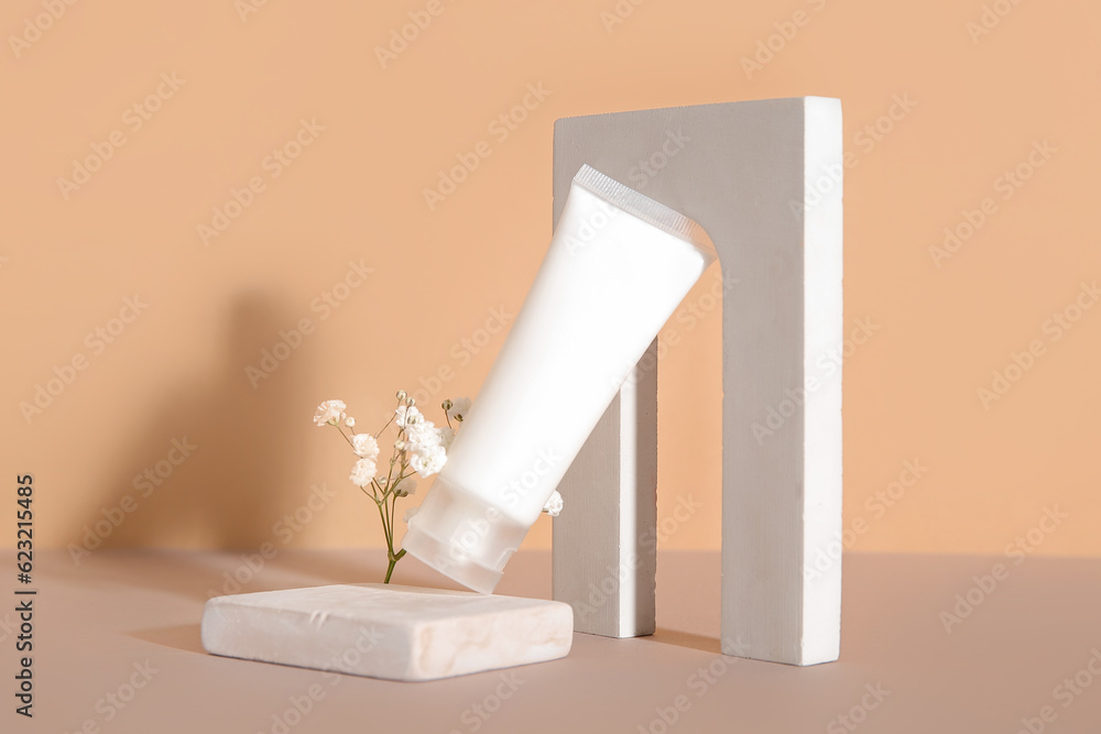 Composition with tube of cosmetic product, plaster podiums and gypsophila flowers on color backgroun