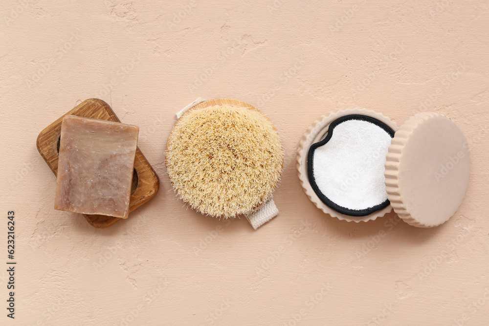 Soap bar, massage brush and cotton pads on color background