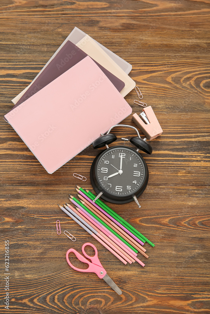 Alarm clock with different stationery on brown wooden background