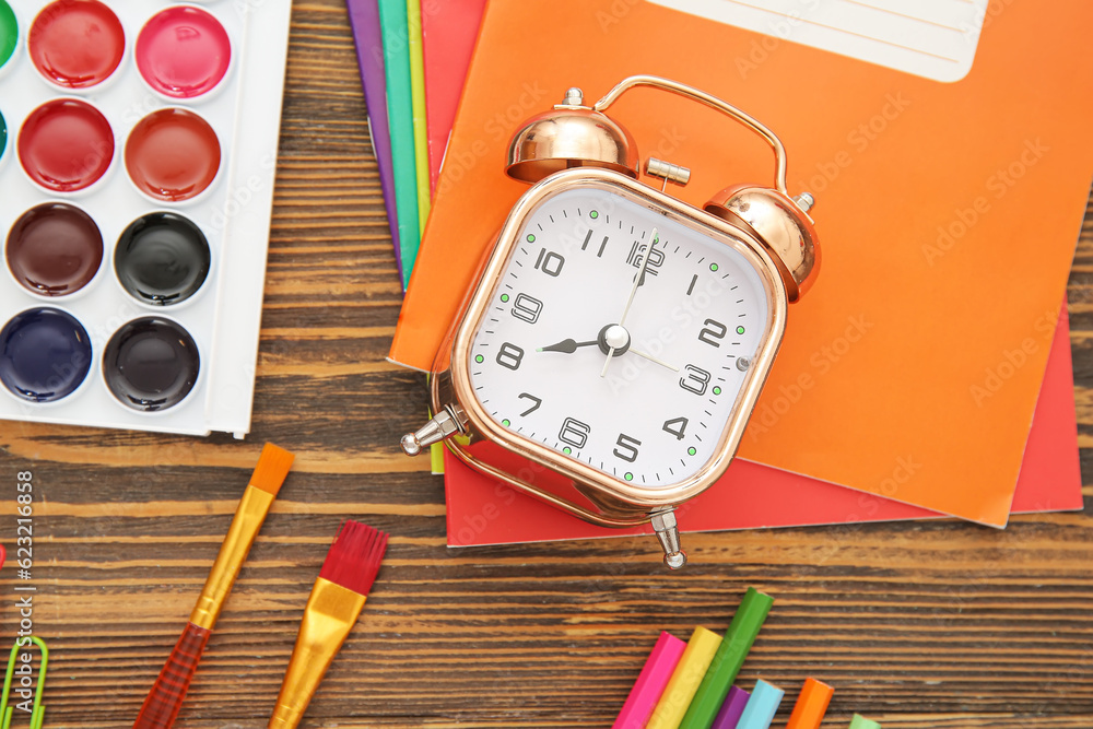 Alarm clock with different stationery on brown wooden background