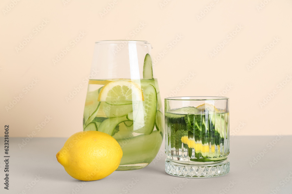 Glass and jug of lemonade with cucumber on grey table