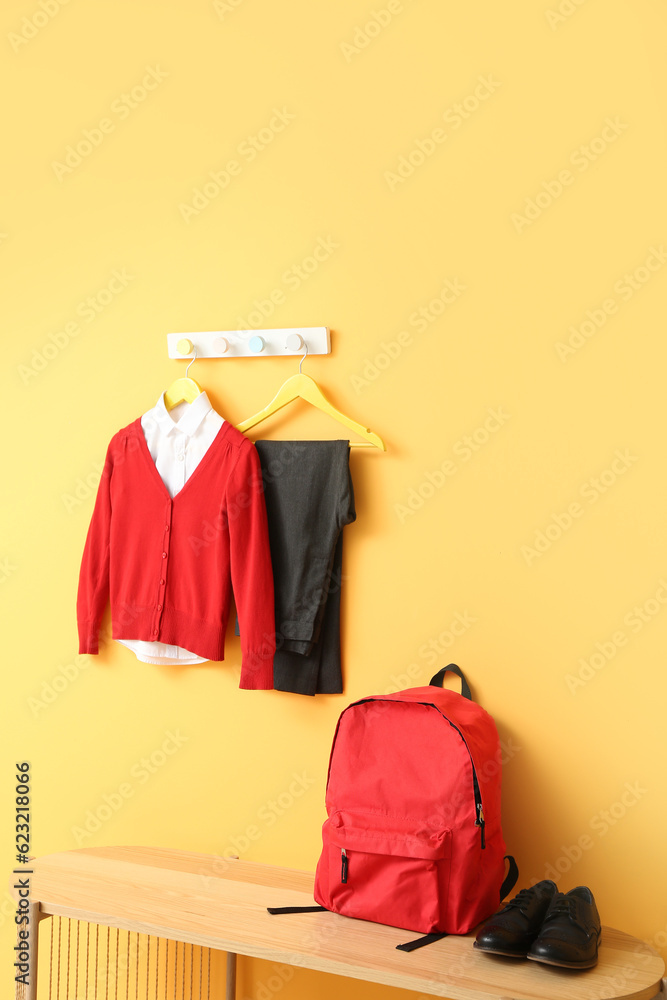 Stylish school uniform hanging on rack with backpack against yellow wall