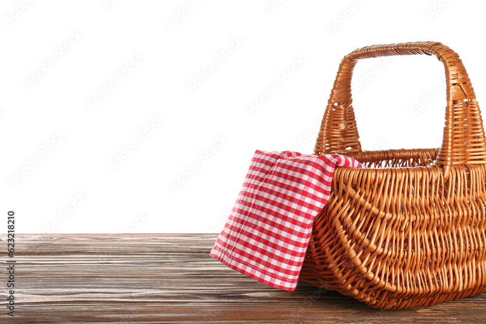 Wicker picnic basket with napkin on wooden table against white background