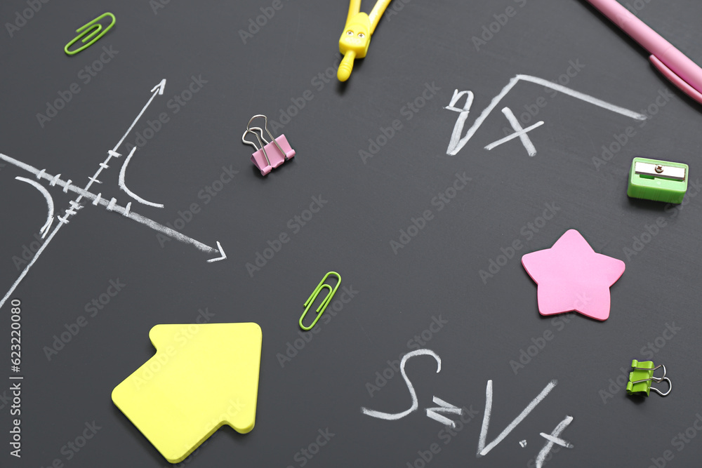 Different stationery on black chalkboard with formulas