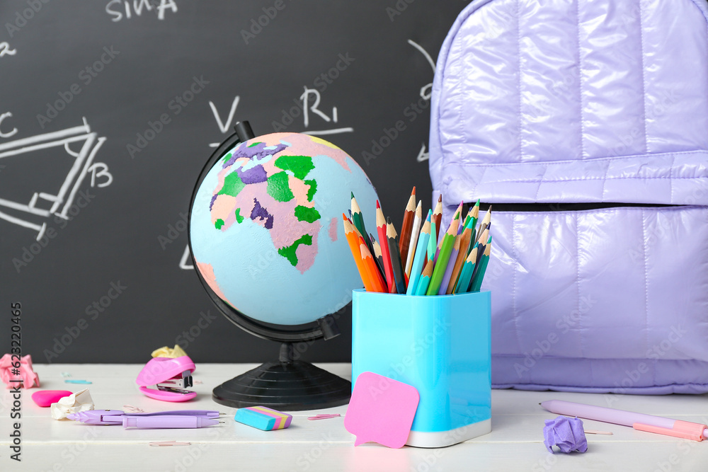 Backpack, stationery and globe on white table against green chalkboard with formulas