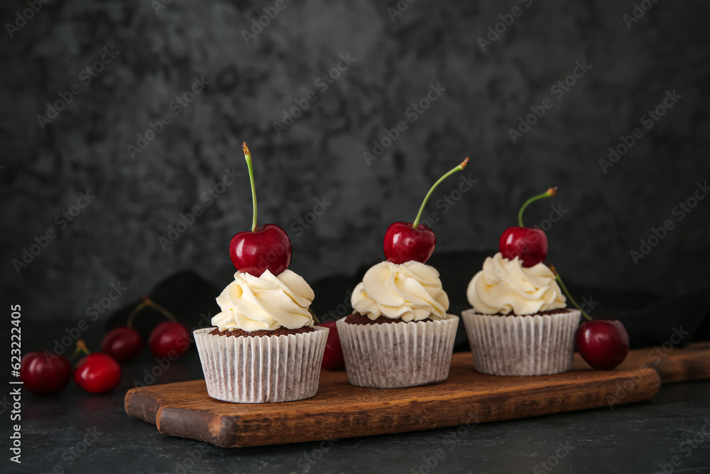 Wooden board with tasty cherry cupcakes on black background