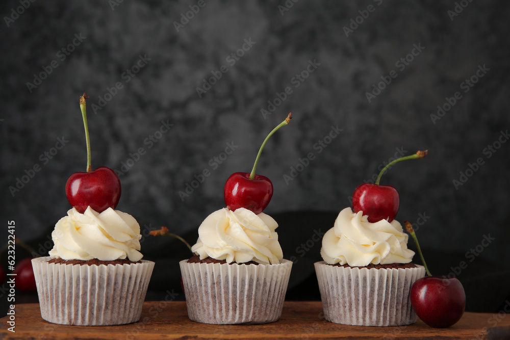 Wooden board with tasty cherry cupcakes on black background