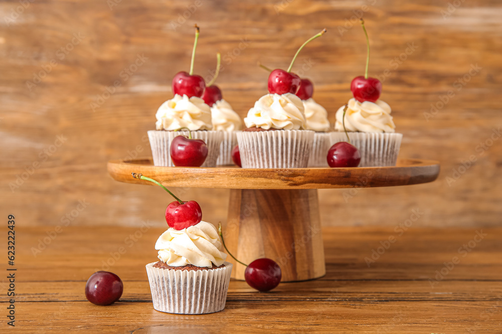 Stand with tasty cherry cupcakes on wooden background