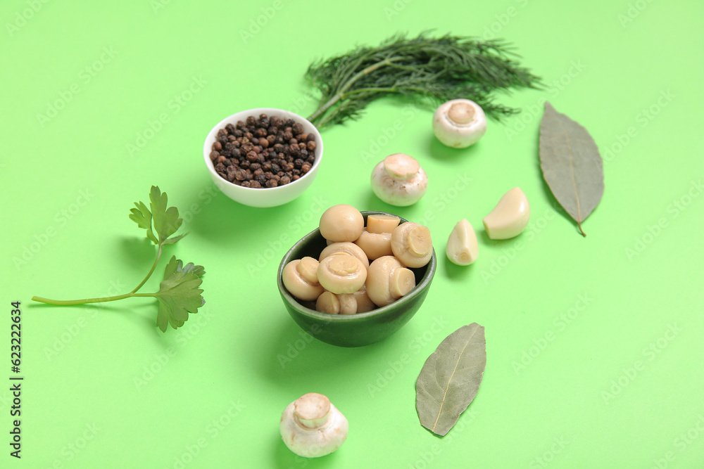 Bowl with canned mushrooms and ingredients for preservation on green background