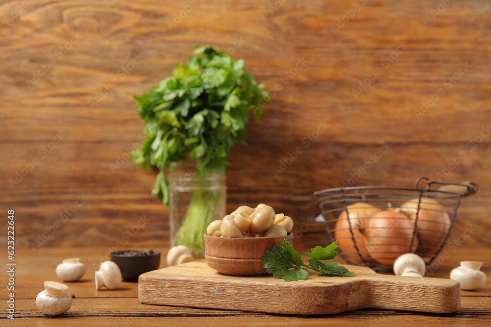 Bowl with canned mushrooms on wooden background