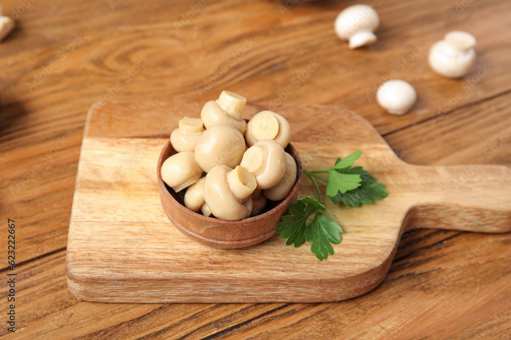 Bowl with canned mushrooms on wooden background