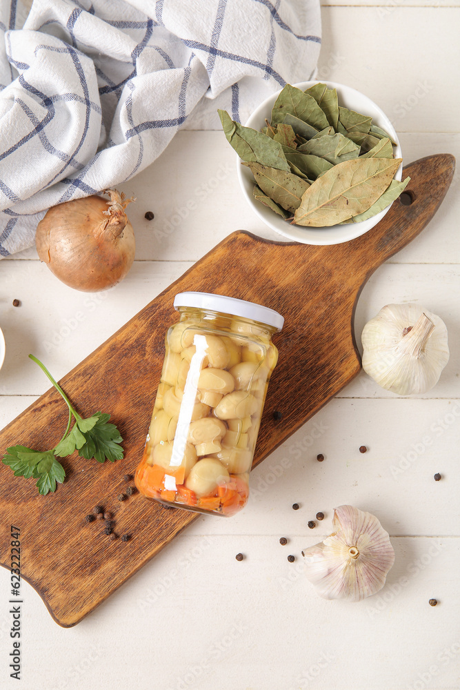 Jar with canned mushrooms and ingredients for preservation on white wooden background