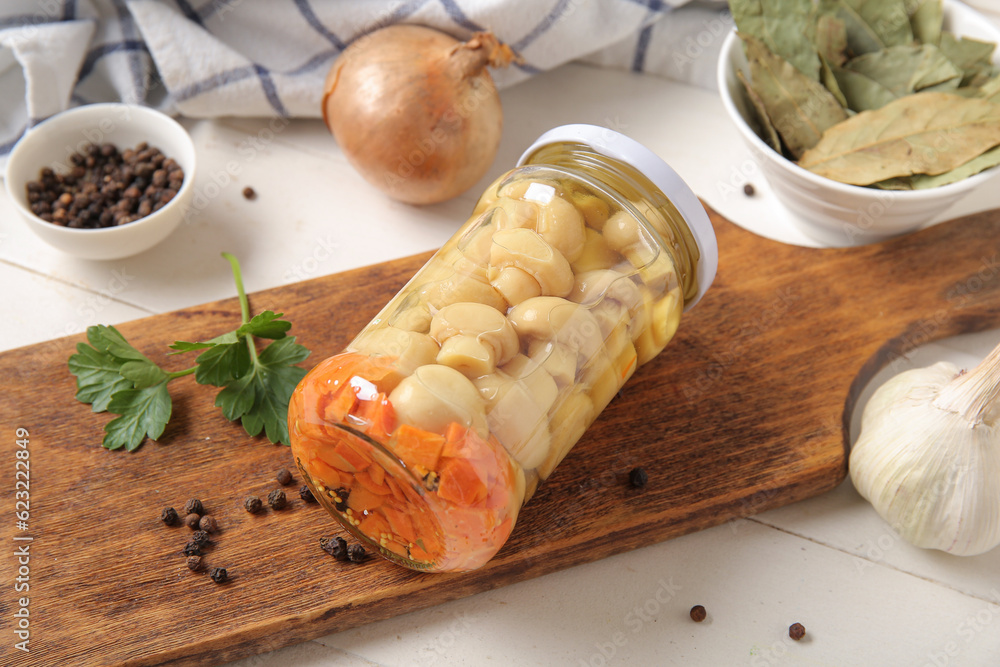 Jar with canned mushrooms and ingredients for preservation on white wooden background