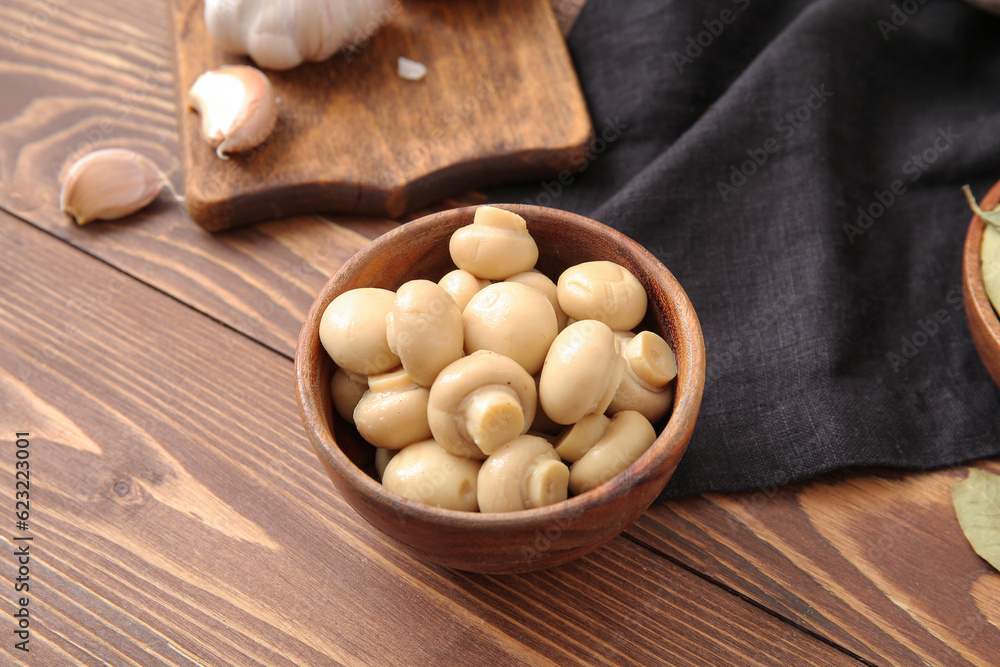 Bowl with canned mushrooms on wooden background