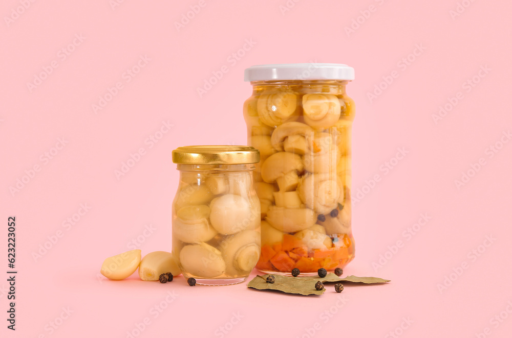 Jars with canned mushrooms on pink background