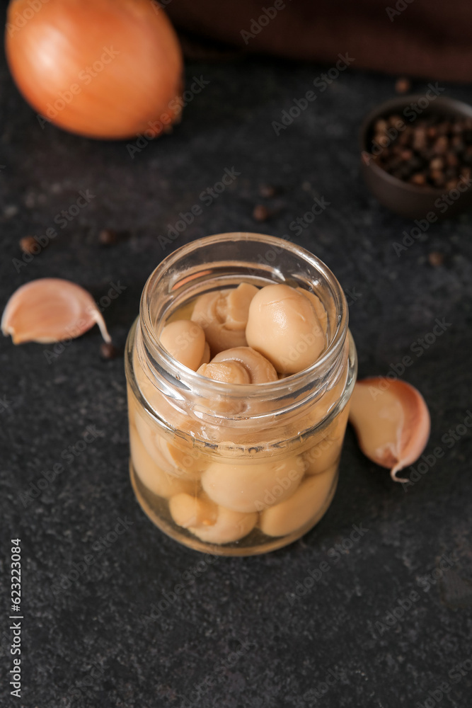 Jar with canned mushrooms on black background