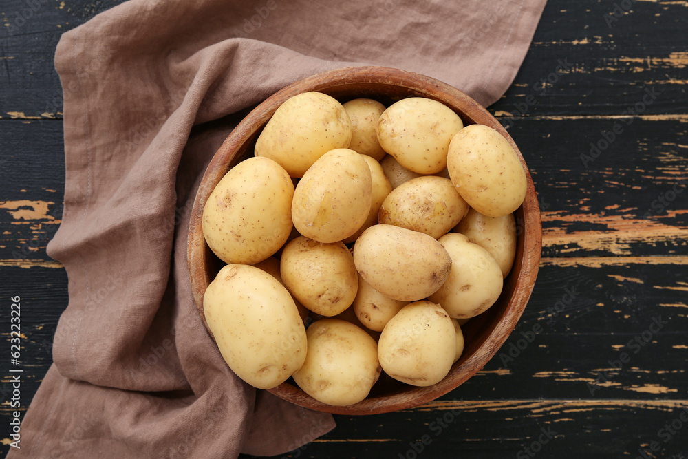 Bowl with raw potatoes on black wooden background