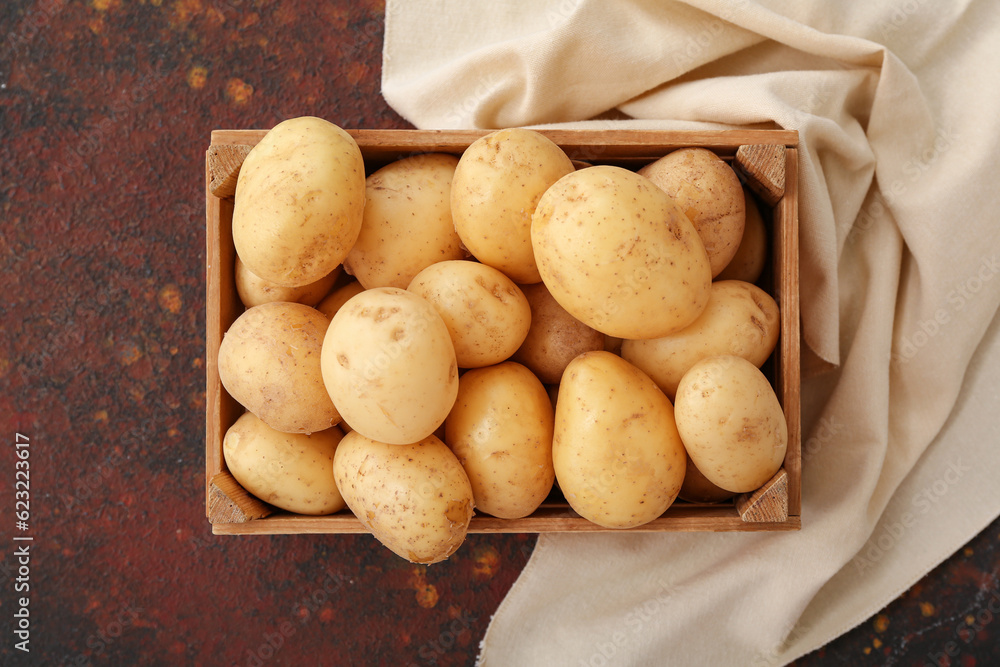 Wooden box with raw potatoes on dark background