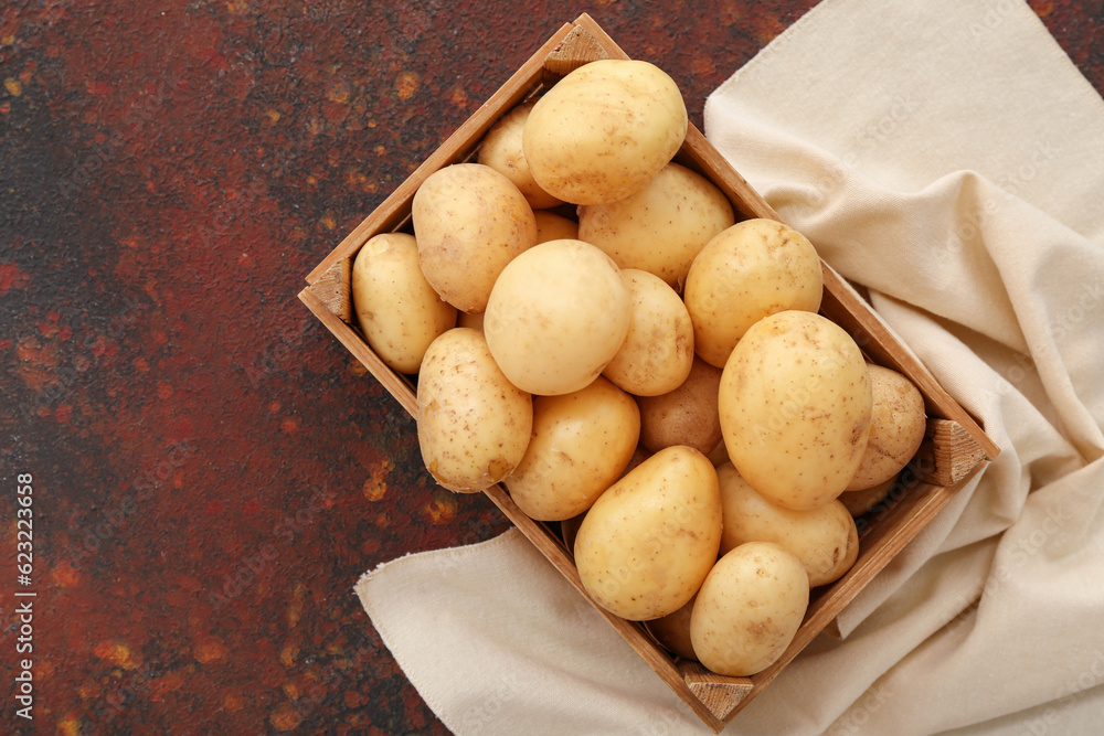 Wooden box with raw potatoes on dark background