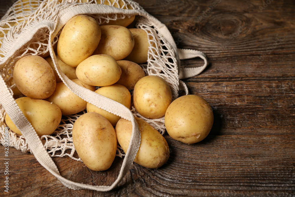 String bag with raw potatoes on wooden table