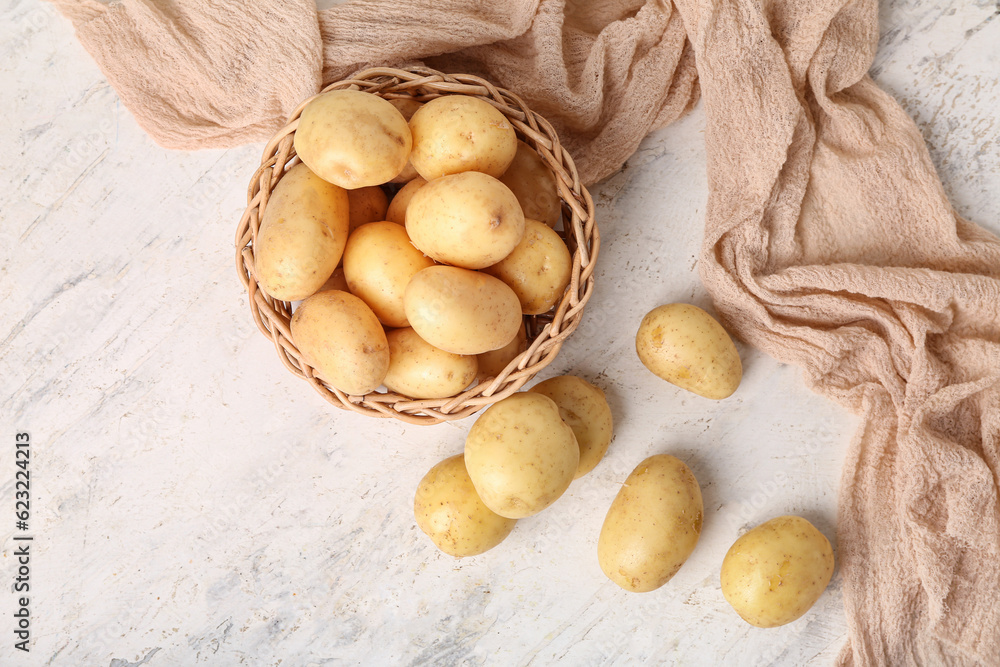 Wicker bowl with raw potatoes on white table