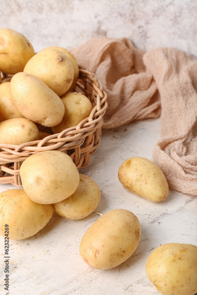 Wicker bowl with raw potatoes on white table