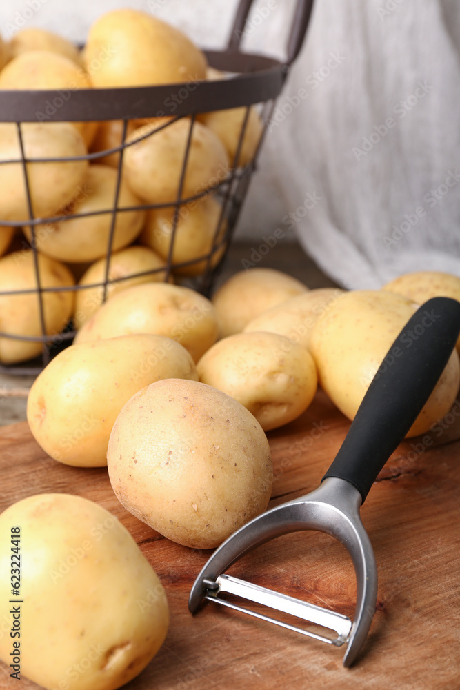 Wooden board and basket with raw potatoes, closeup