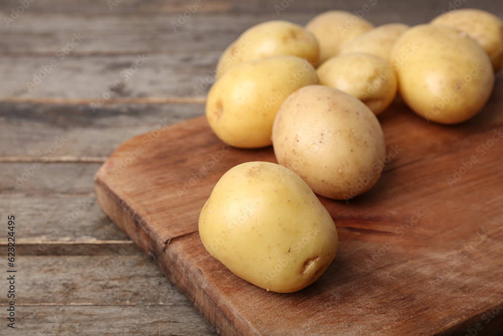 Board with raw potatoes on wooden table, closeup