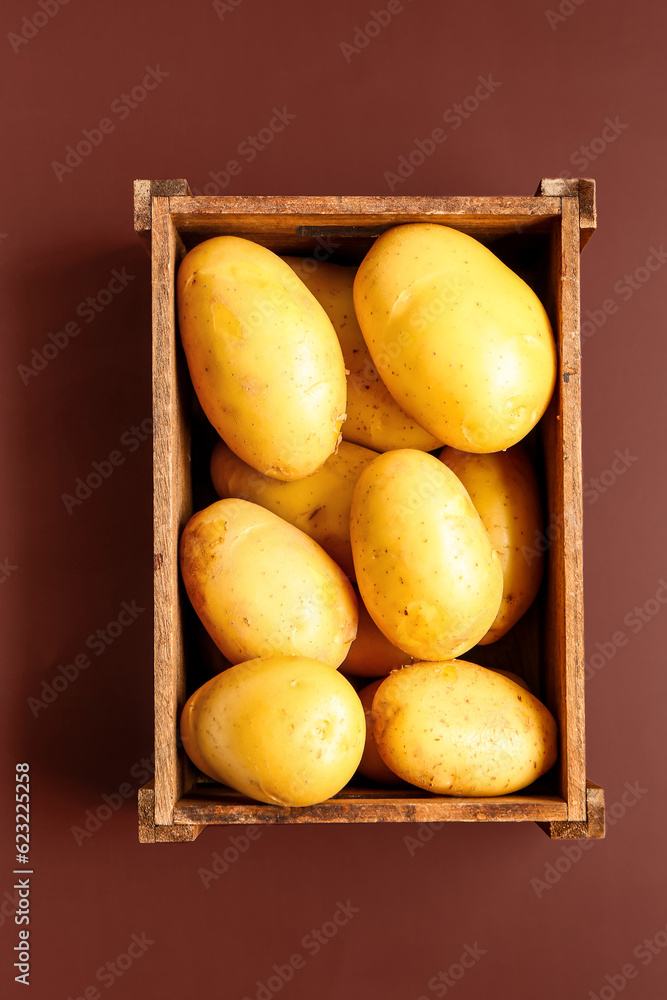 Wooden box with raw potatoes on brown background