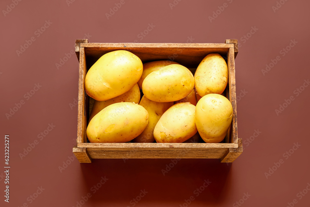 Wooden box with raw potatoes on brown background