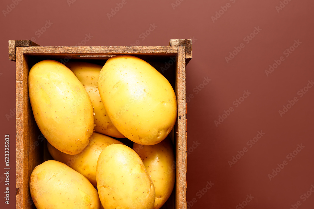 Wooden box with raw potatoes on brown background