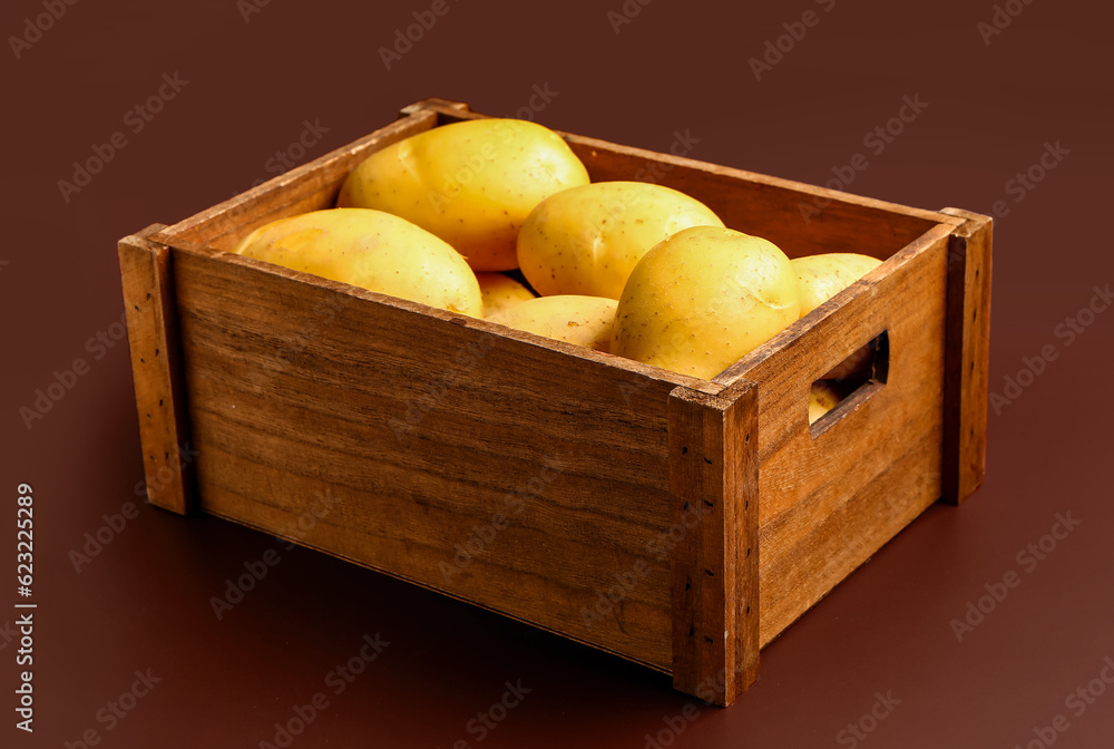 Wooden box with raw potatoes on brown background