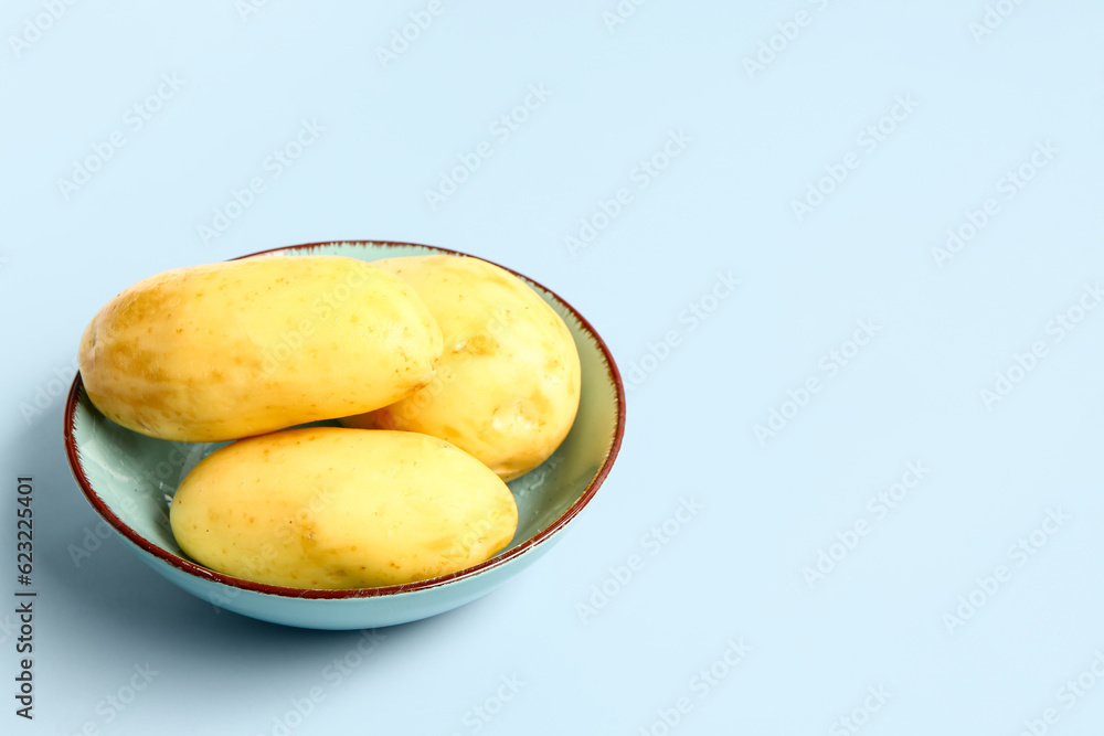 Bowl with raw potatoes on blue background