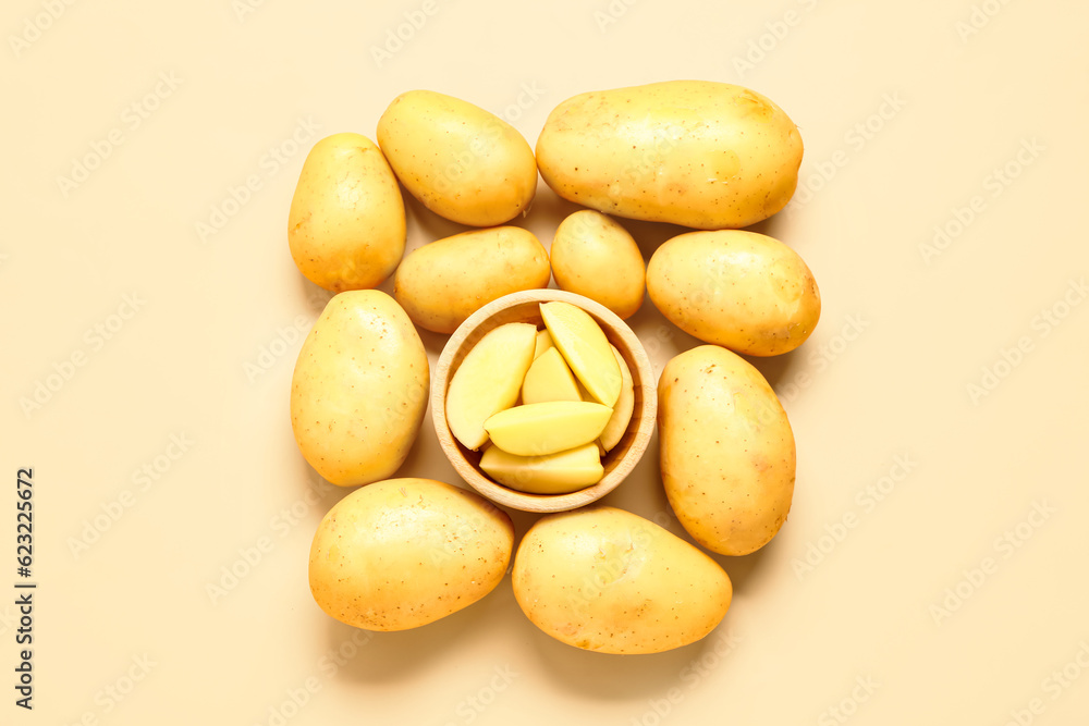 Bowl with cut and whole potatoes on yellow background